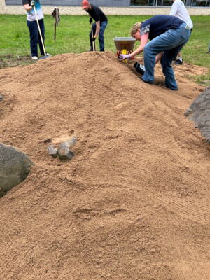 Schülerinnen entnehmen einem Sandhaufen Sand.