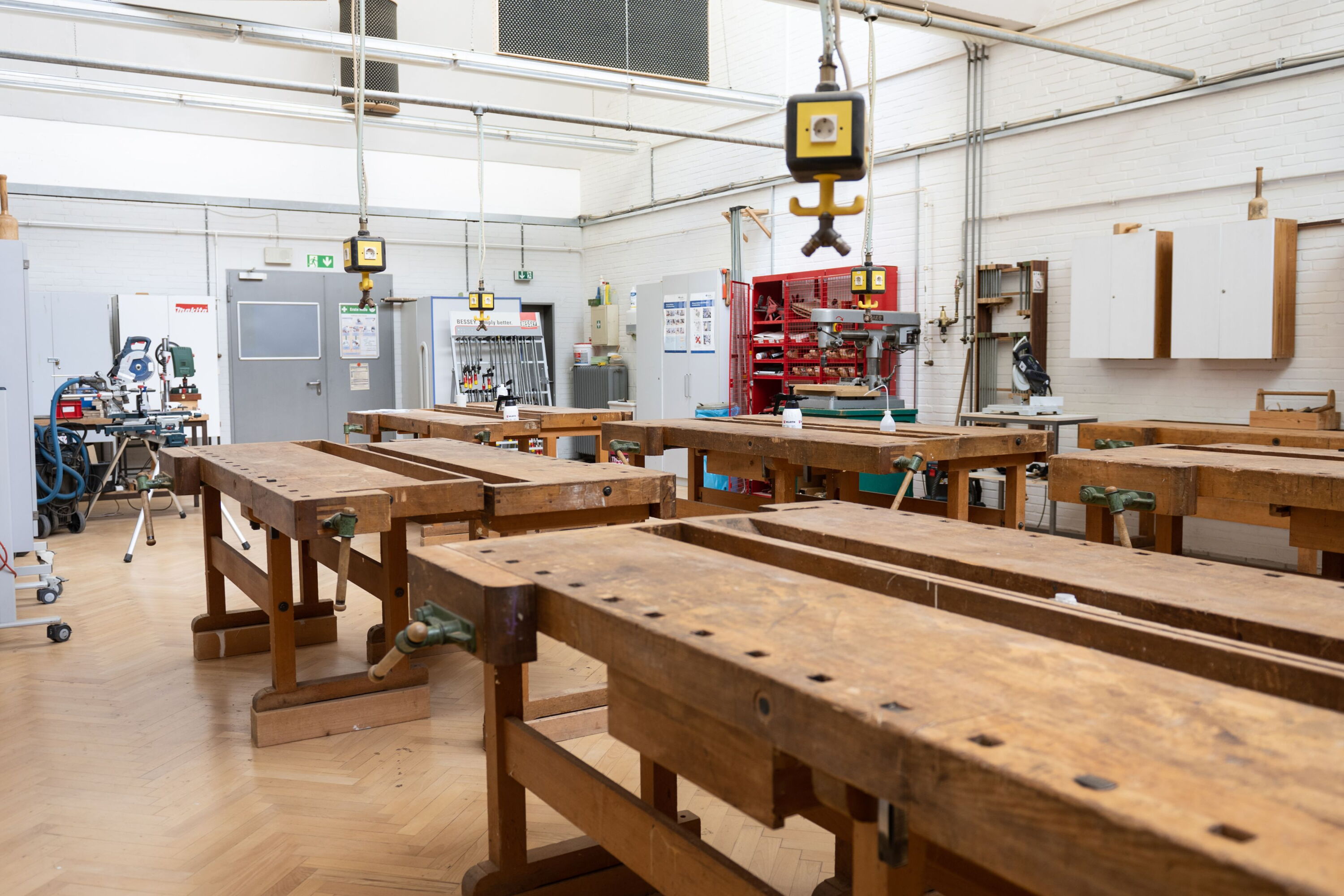 Werkhalle mit mehreren Werkbänken aus Holz und Steckdosen von der Decke hängend.