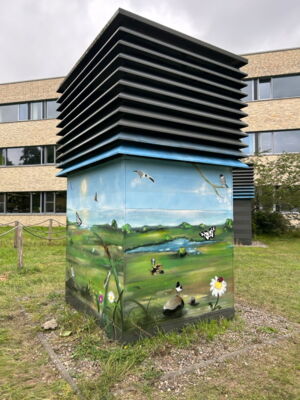 Die fertig besprühte Entlüftungsanlage mit Wiesen, Insekten und einem See.