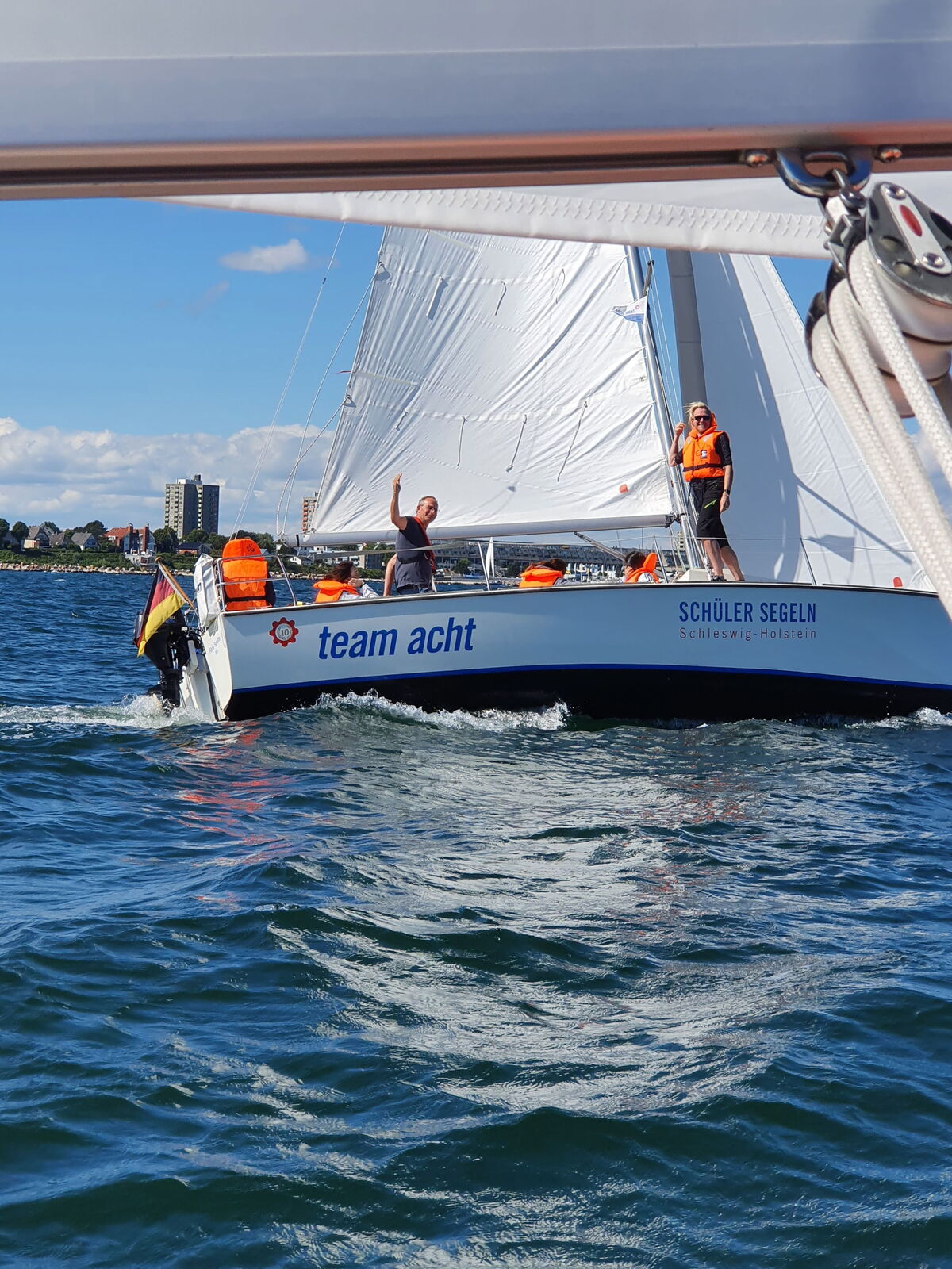 Schräg liegendes Segelboot mit winkendem Bootsführer.