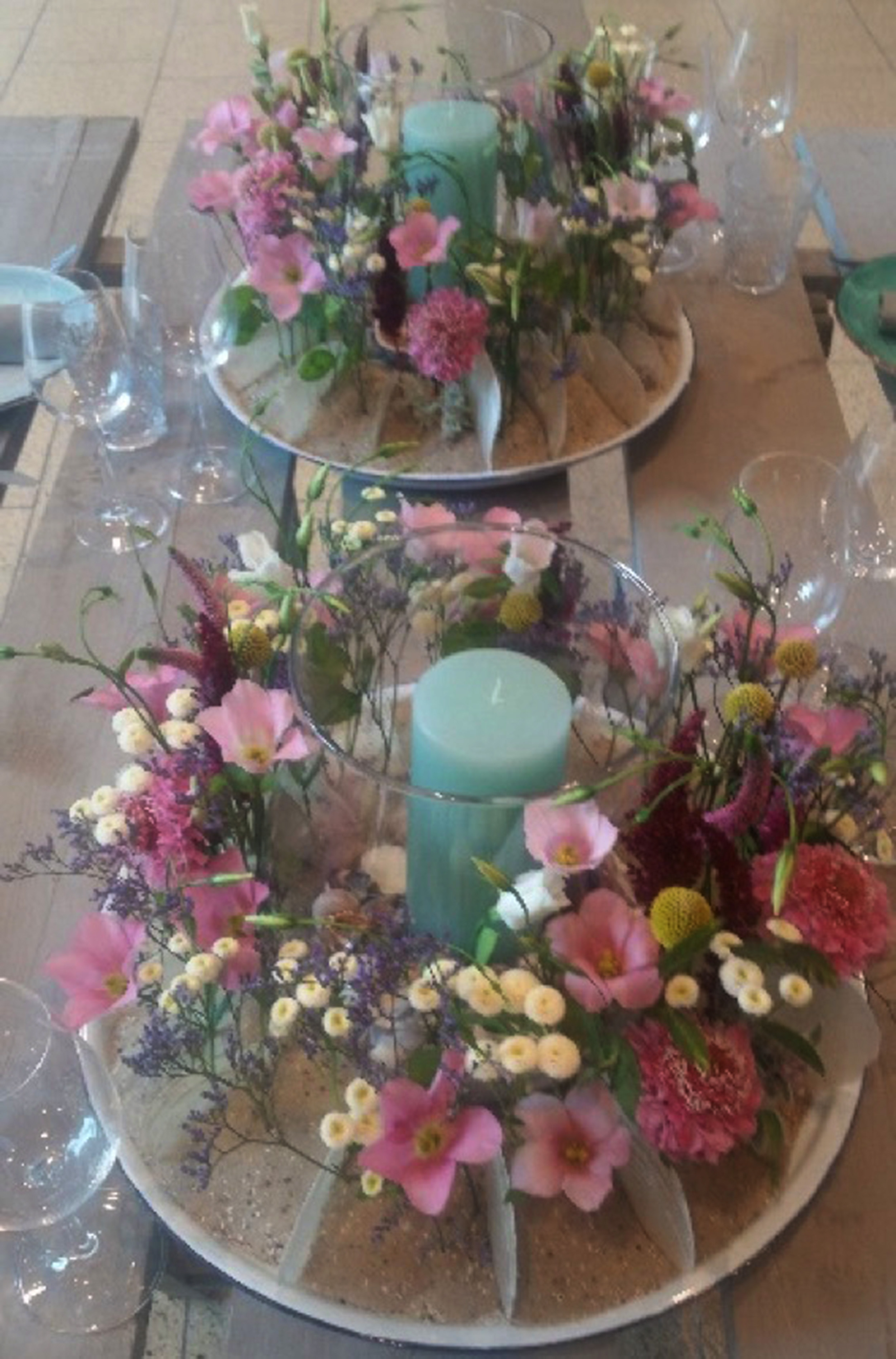 Zwei Blumenarrangements mit jeweils einer Kerze im Zentrum.