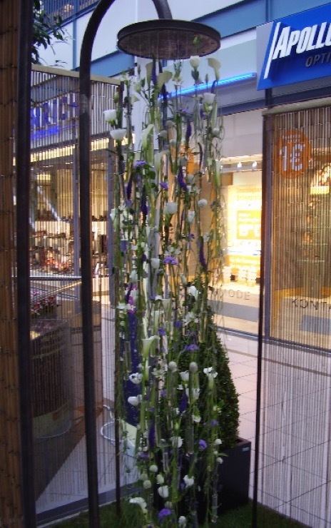 Im Einkaufszentrum kommen aus einer Dusche scheinbar Blumen und Pflanzen statt Wasser.