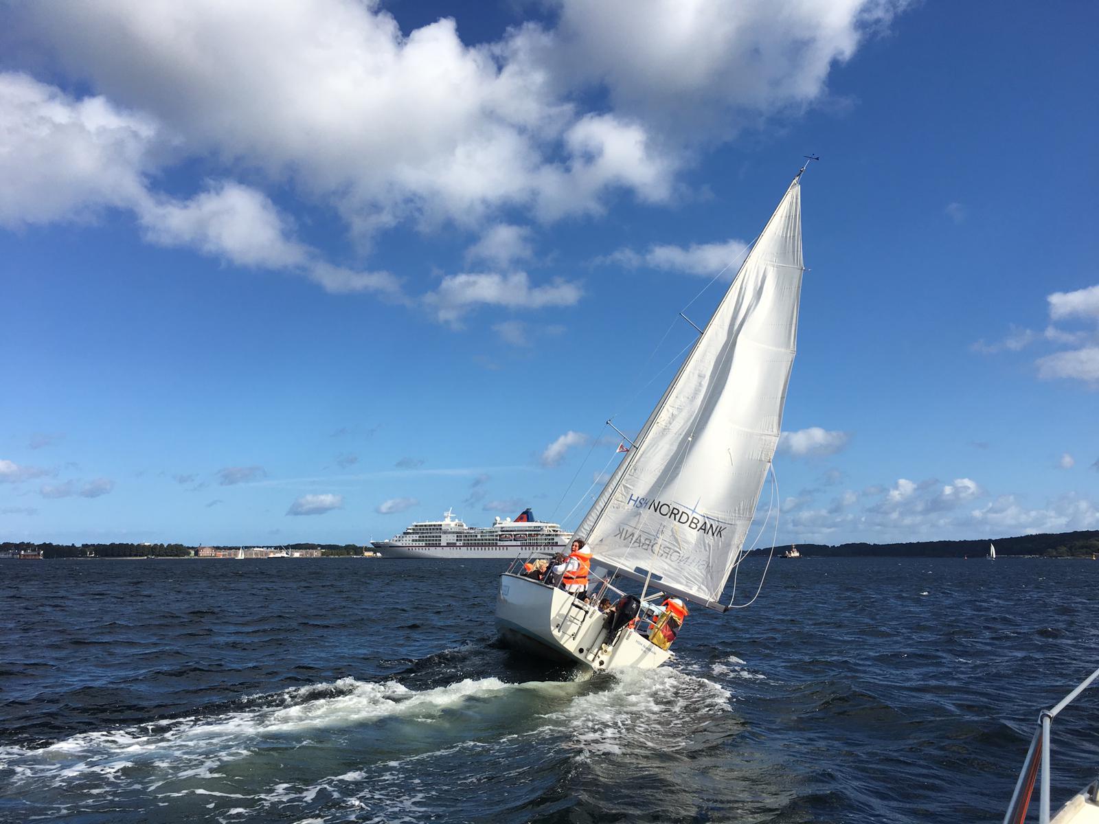 Detailansicht eines Segelbootes auf der  Kieler Förde, im Hintergrund ein Passagierschiff.